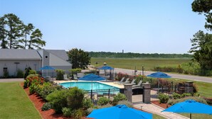 A swimming pool with lounge chairs and umbrellas, surrounded by a landscaped garden and a building. - Spark by Hilton Chincoteague Island (Chincoteague)