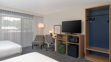 Et hotelværelse med seng, skrivebord med computer, fjernsyn, stol, skraldespand og et klædeskab.