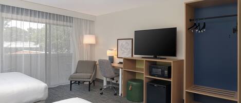 Ett hotellrum med en säng, ett skrivbord med en dator, en tv, en stol, en papperskorg och en garderob.