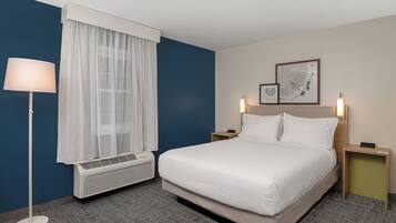 A hotel room with a bed, a standing lamp, a window with curtains, an air conditioner, and two bedside tables with lamps.