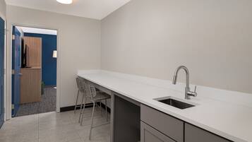 A modern kitchen with a white countertop, a built-in sink, and a chair.
