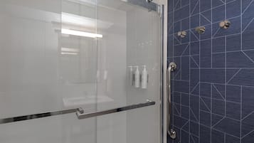 A modern bathroom with a glass shower enclosure, a metallic handle, and a blue tiled wall with geometric patterns.