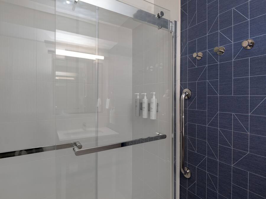 A modern bathroom with a glass shower enclosure, a metallic handle, and a blue tiled wall with geometric patterns.