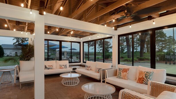 A spacious indoor area with a white sofa set, round tables, and large windows offering views of the outdoors. - Spark by Hilton Chincoteague Island (Chincoteague)