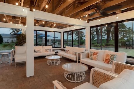 A spacious indoor area with a white sofa set, round tables, and large windows offering views of the outdoors.