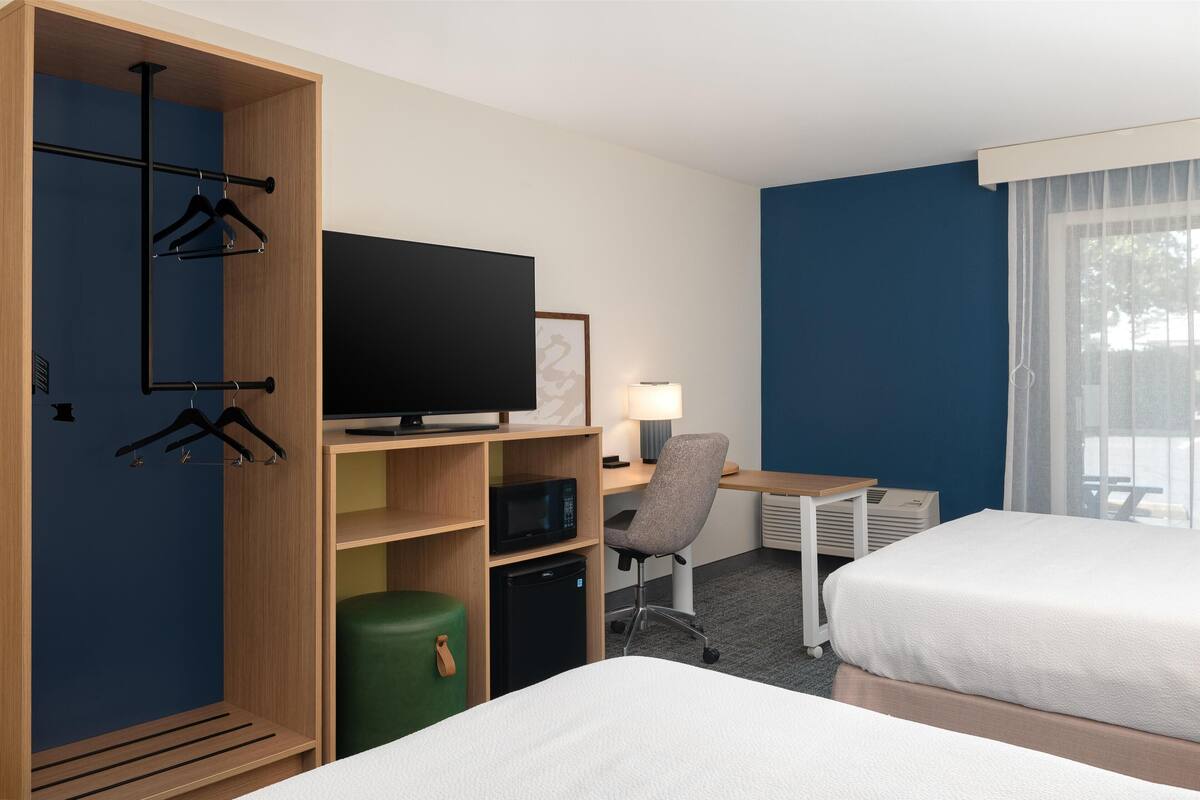 A hotel room with a bed, a desk with a computer, a television, a chair, and a wardrobe with hangers.
