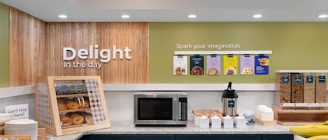 A kitchen area with a microwave, a doughnut display, and a sign that reads 'Delight in the day'.
