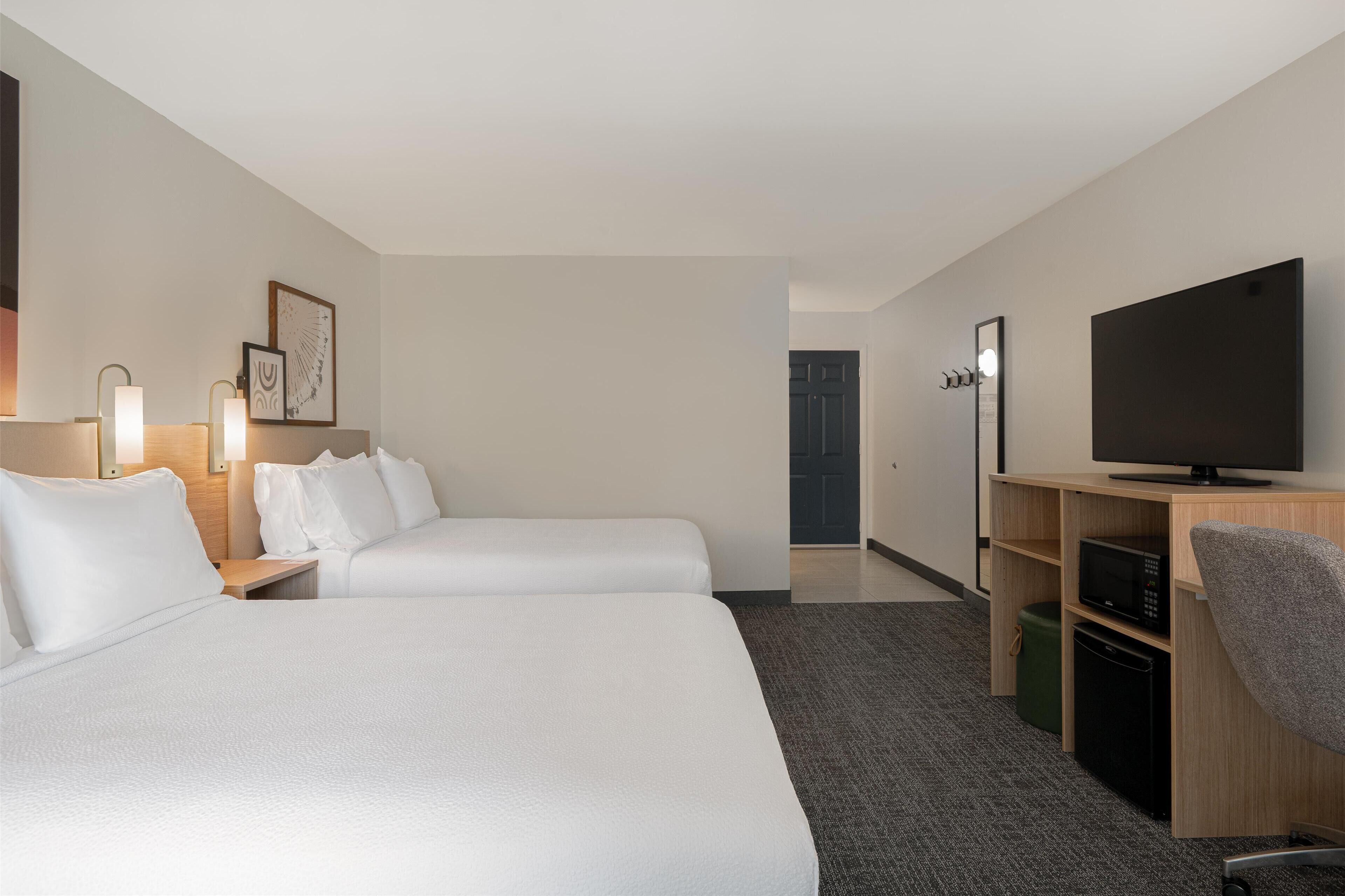 Een hotelkamer met twee bedden, een televisie, een bureau met een magnetron en een prullenbak.