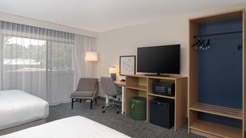 Quarto de hotel com cama, escrivaninha com computador, televisão, cadeira, cabideiro e guarda-roupa.