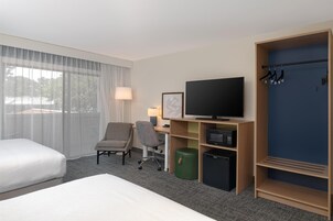 Quarto de hotel com cama, escrivaninha com computador, televisão, cadeira, cabideiro e guarda-roupa.