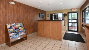 A reception area with a wooden reception desk, a bulletin board with various items, and an exit sign. - Ardsley Acres Hotel Westchester (Ardsley)