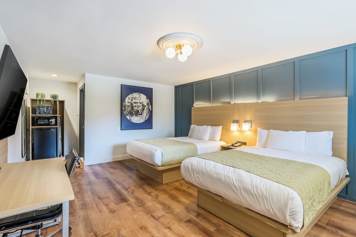 A hotel room with two beds, a desk, a TV, and a bookshelf.