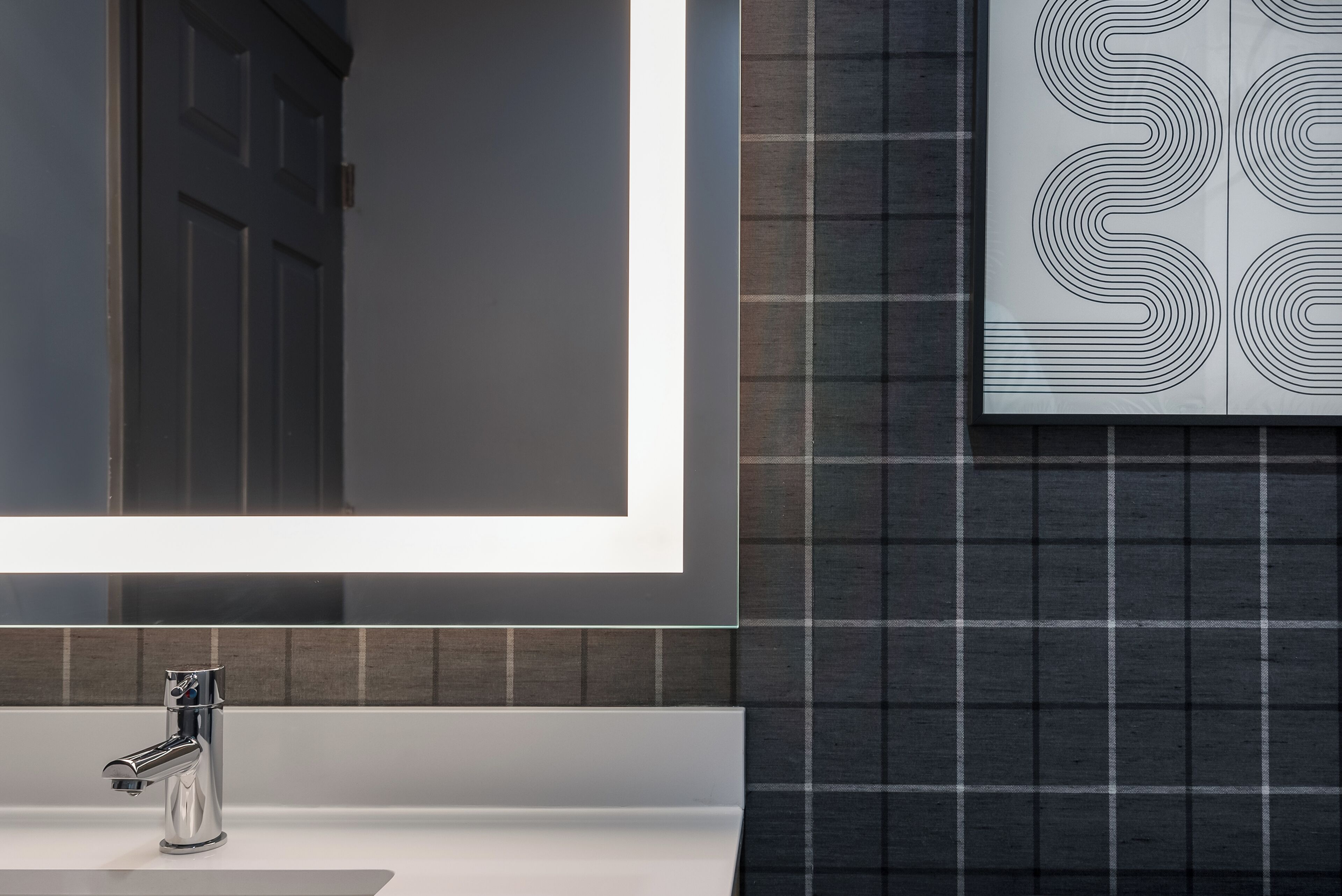 Un baño moderno con un espejo grande, un grifo cromado y un papel tapiz estampado.