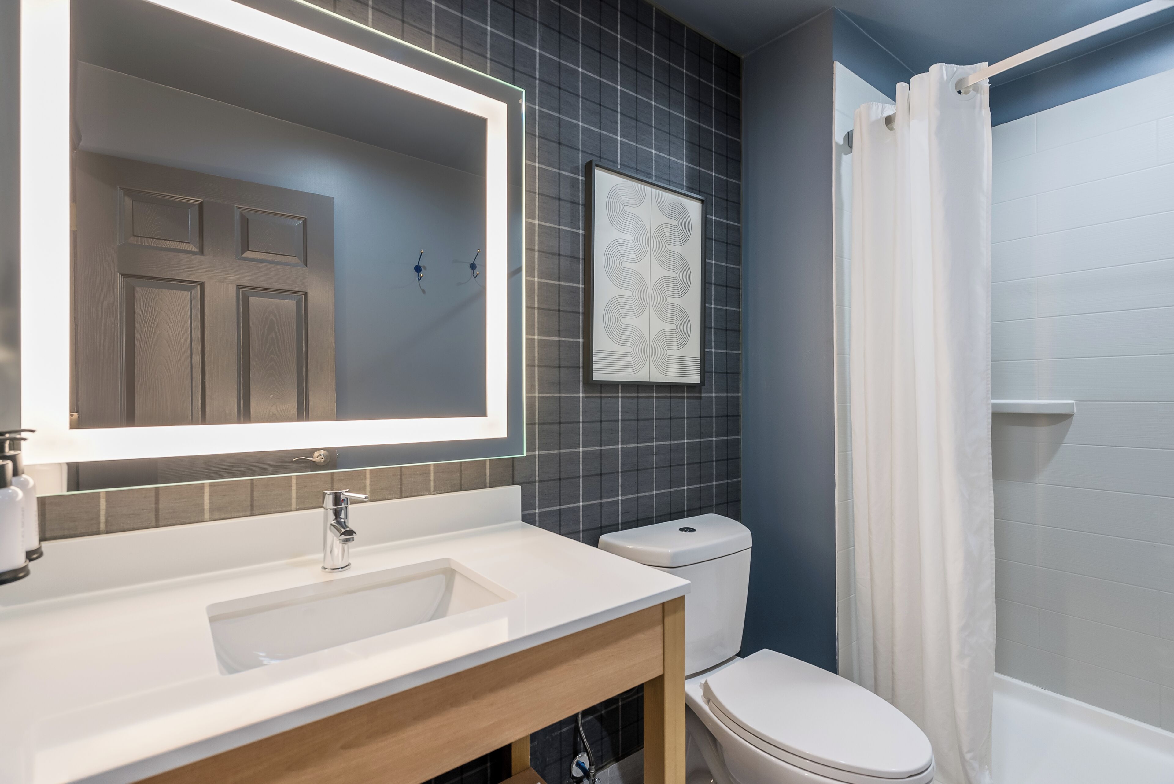 A modern bathroom with a white sink, a mirror, a toilet, and a shower curtain.