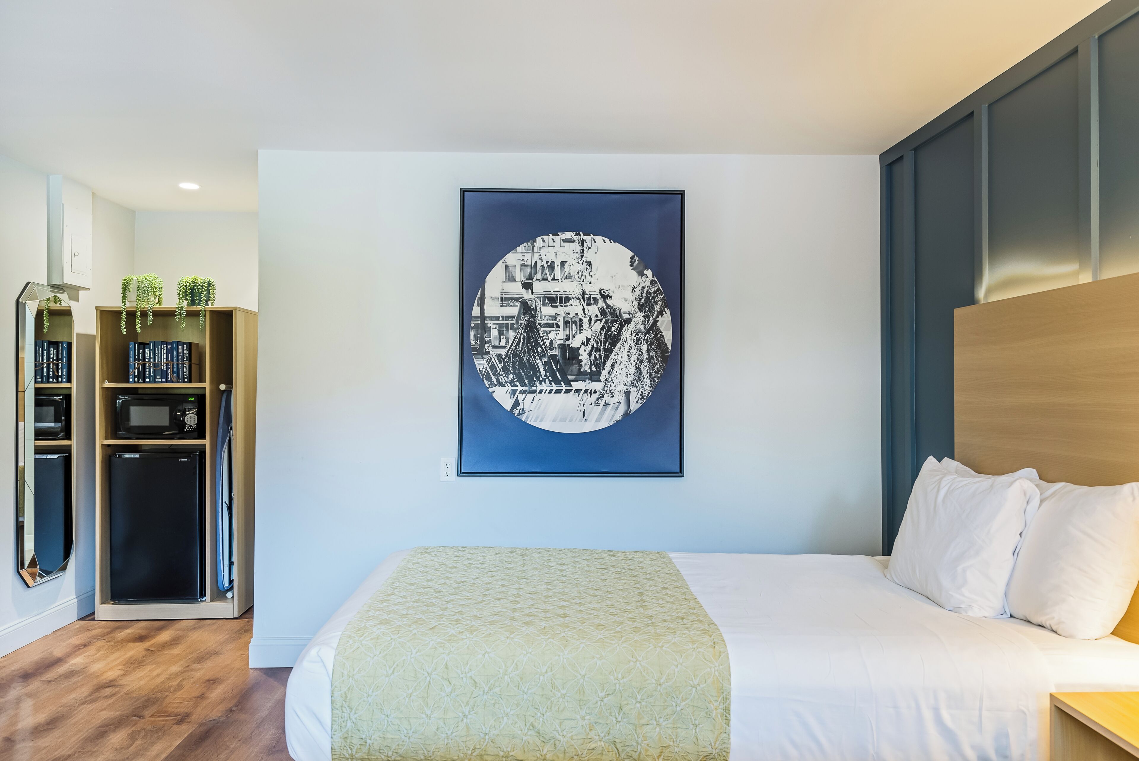 A hotel room with a bed, a wall-mounted artwork, a built-in bookshelf, and a microwave.