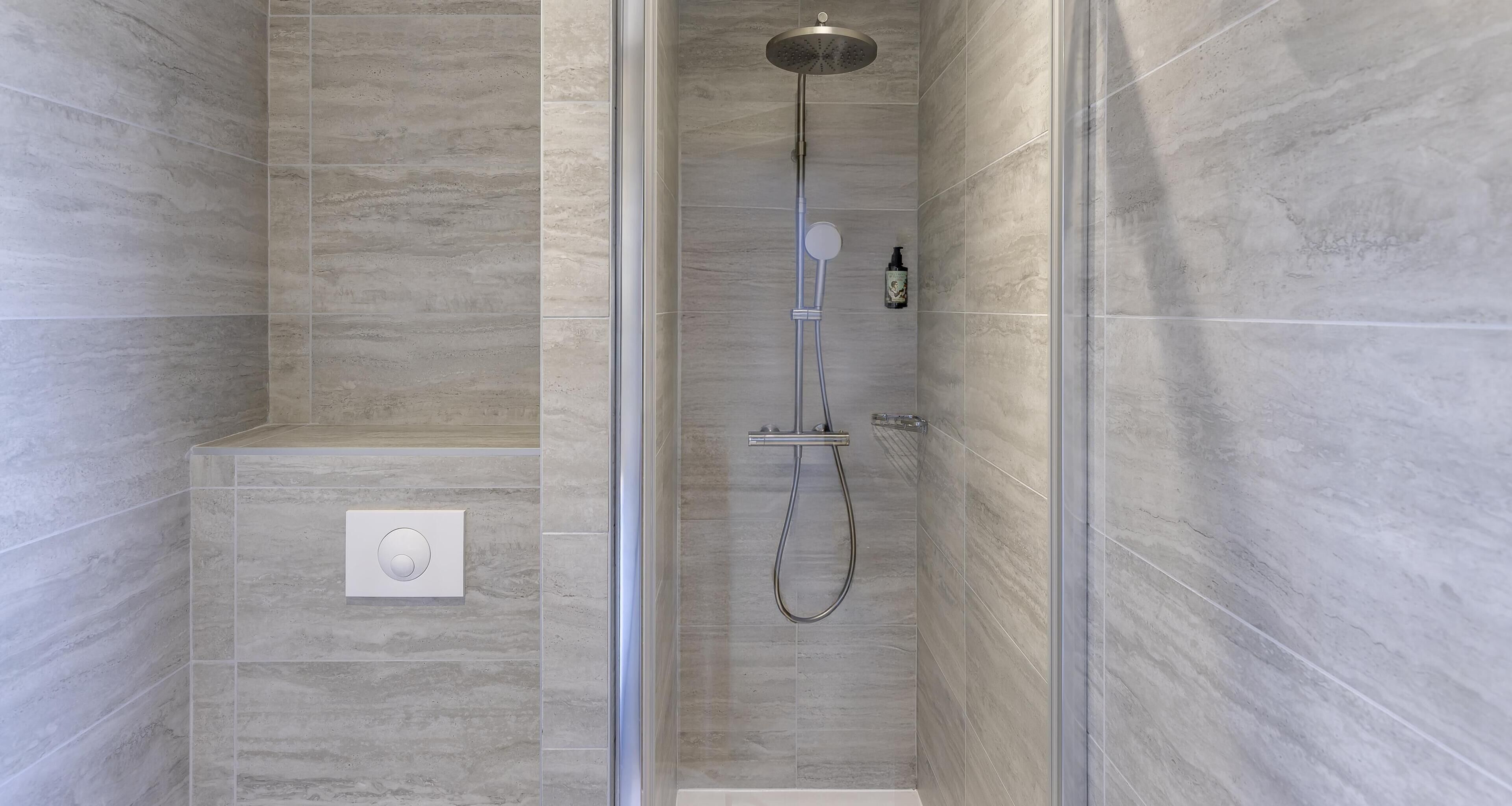 A modern shower with a glass door, a handheld showerhead, and a wall-mounted control panel.