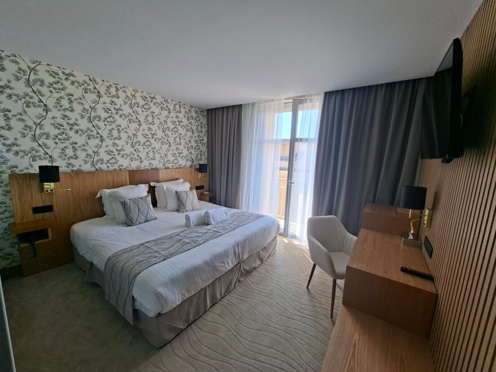 A hotel room with a large bed, a desk, a chair, and a TV mounted on the wall.