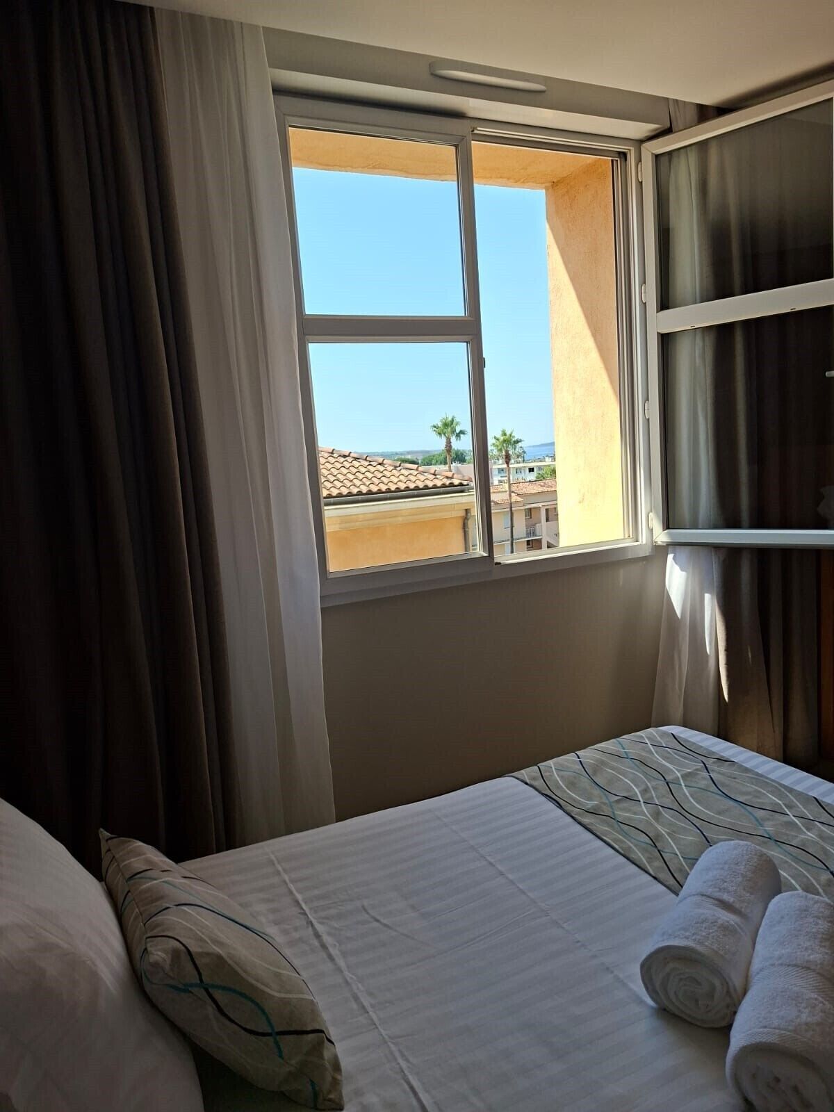A hotel room with a bed, a window with curtains, and a view of the outside.