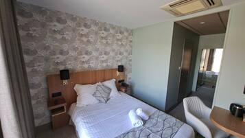 A hotel room with a bed, two bedside tables, a chair, and a small table with a kettle.