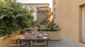 Una mesa de madera con sillas, un plato de comida y un vaso de jugo en un balcón con una escalera de piedra y plantas.
