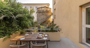 Una mesa de madera con sillas, un plato de comida y un vaso de jugo en un balcón con una escalera de piedra y plantas.