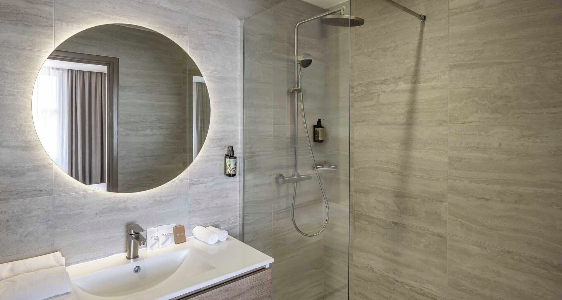 Ein modernes Badezimmer mit rundem Spiegel, Waschbecken und Dusche.