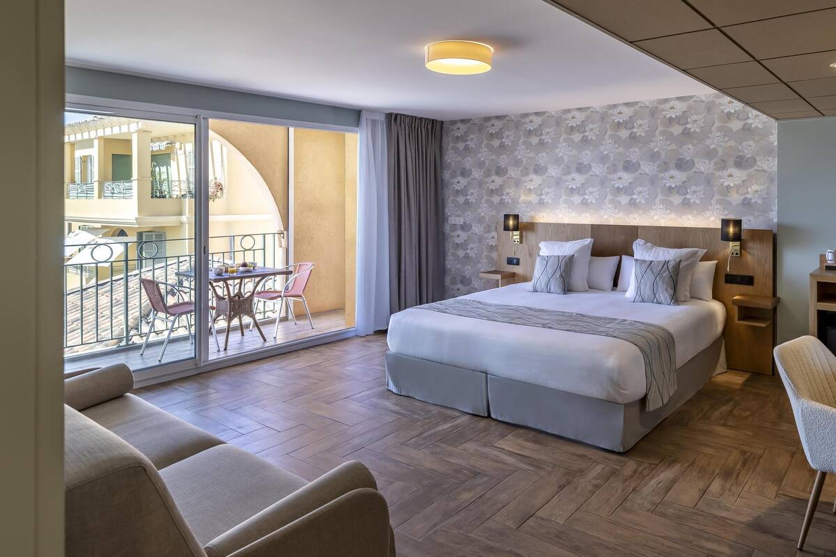 Una habitación de hotel moderna con una cama grande, un escritorio y un balcón con mobiliario exterior.