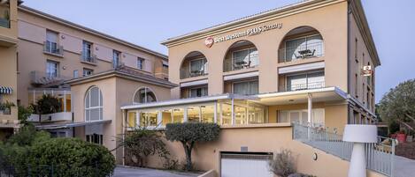 A hotel with a beige facade, multiple balconies, and a sign reading "Best Western PLUS Sanary".