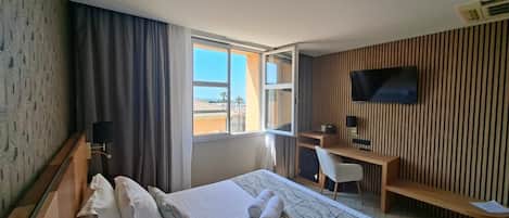 A hotel room with a bed, a desk, a TV, and a window with a view of buildings.