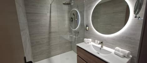 A modern bathroom with a walk-in shower, a large mirror, and a vanity with a sink and towel rack.
