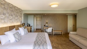 Habitación de hotel con una cama grande, un escritorio, una silla, un sofá y un baño visible a través de una puerta abierta.