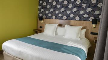 A hotel room with a bed, a nightstand, and a wall with a floral wallpaper pattern.