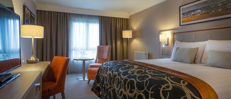 Una habitación de hotel con cama, escritorio, silla, mesa y televisión.