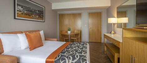 A hotel room with a bed, a desk, a chair, a lamp, and a television.