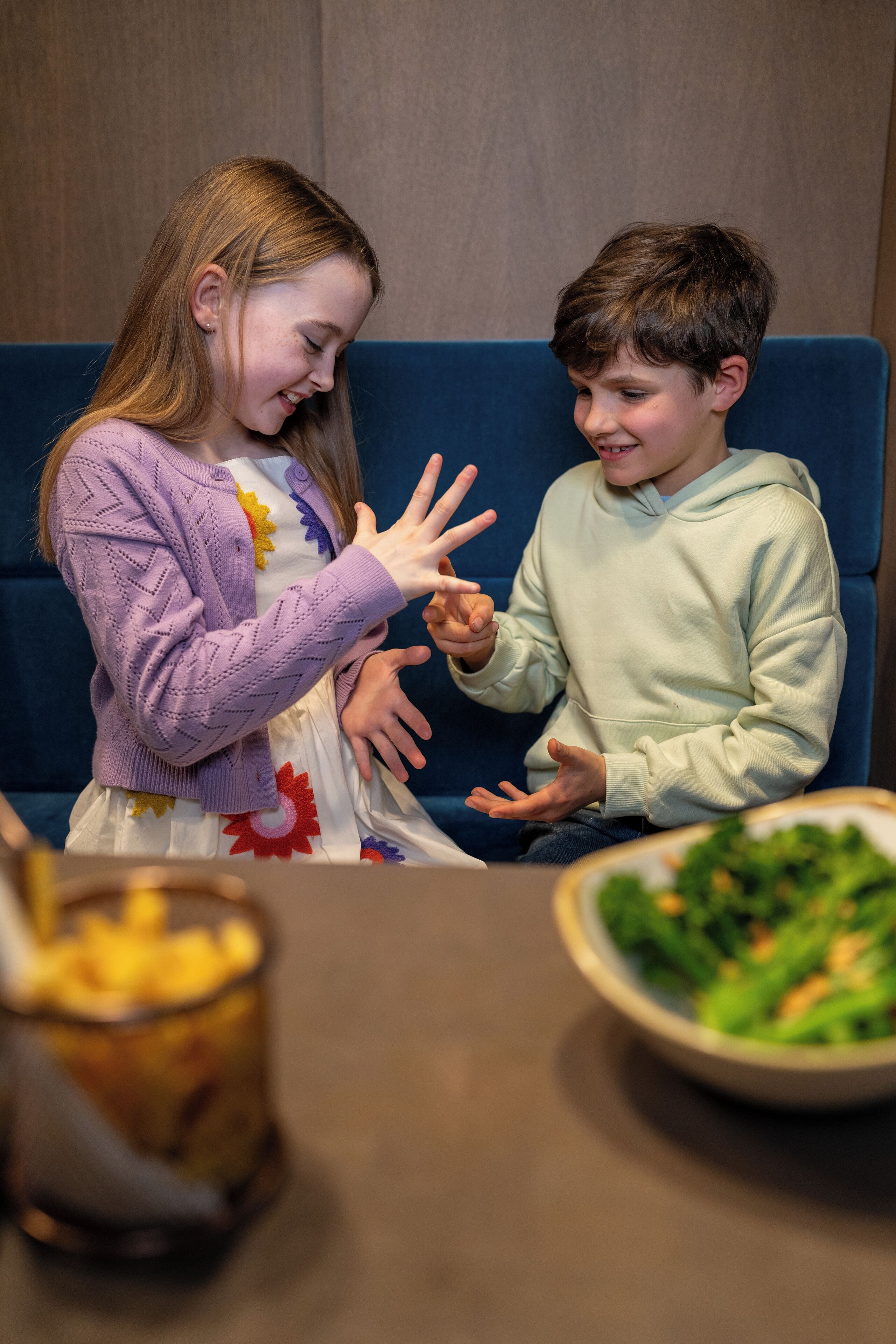 Dos personas sentadas en un sofá azul con un tazón de ensalada y un vaso de bebida sobre la mesa.