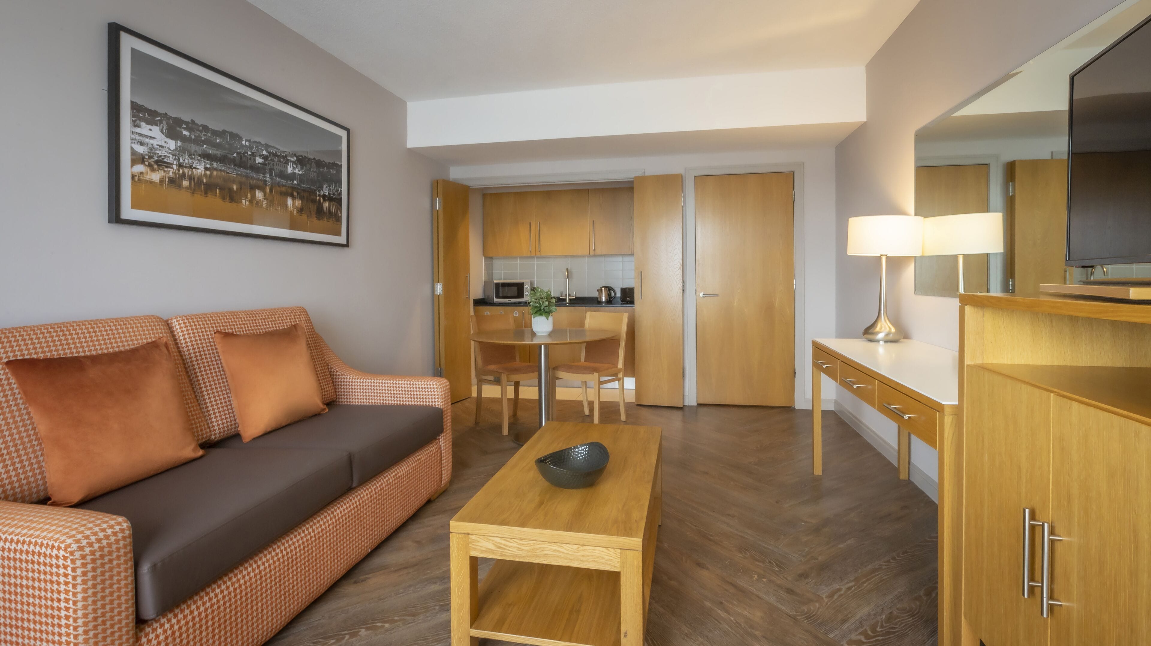 Un salon moderne comprenant un canapé, une table basse et un coin repas avec une table et des chaises. Il y a également un coin cuisine avec des placards et un four à micro-ondes.