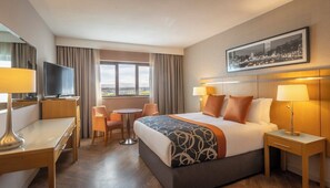 A hotel room with a bed, two bedside tables, a desk, a chair, a TV, and a window with curtains.