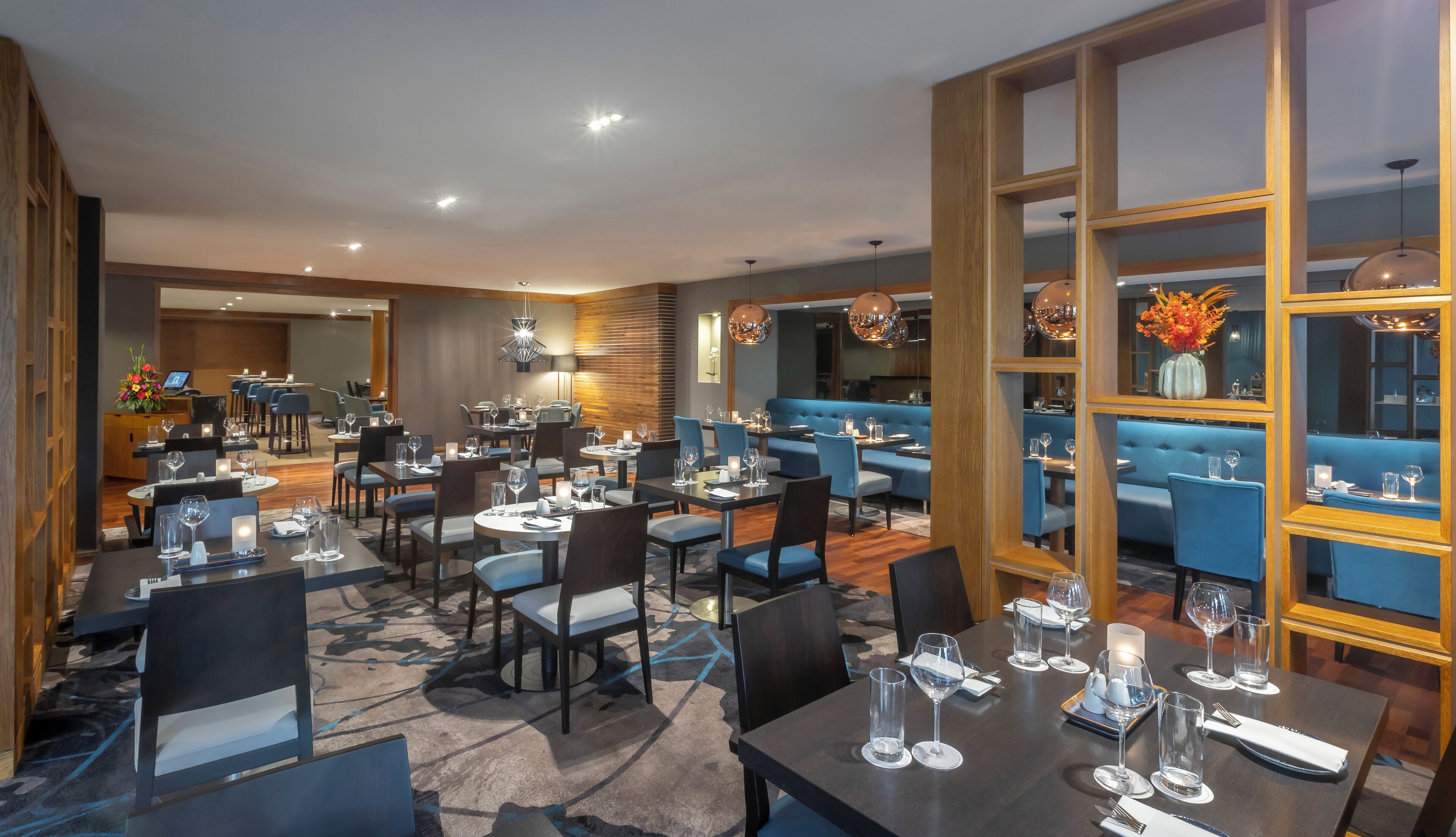 A modern restaurant with multiple dining areas, including booths and tables, and a bar area.