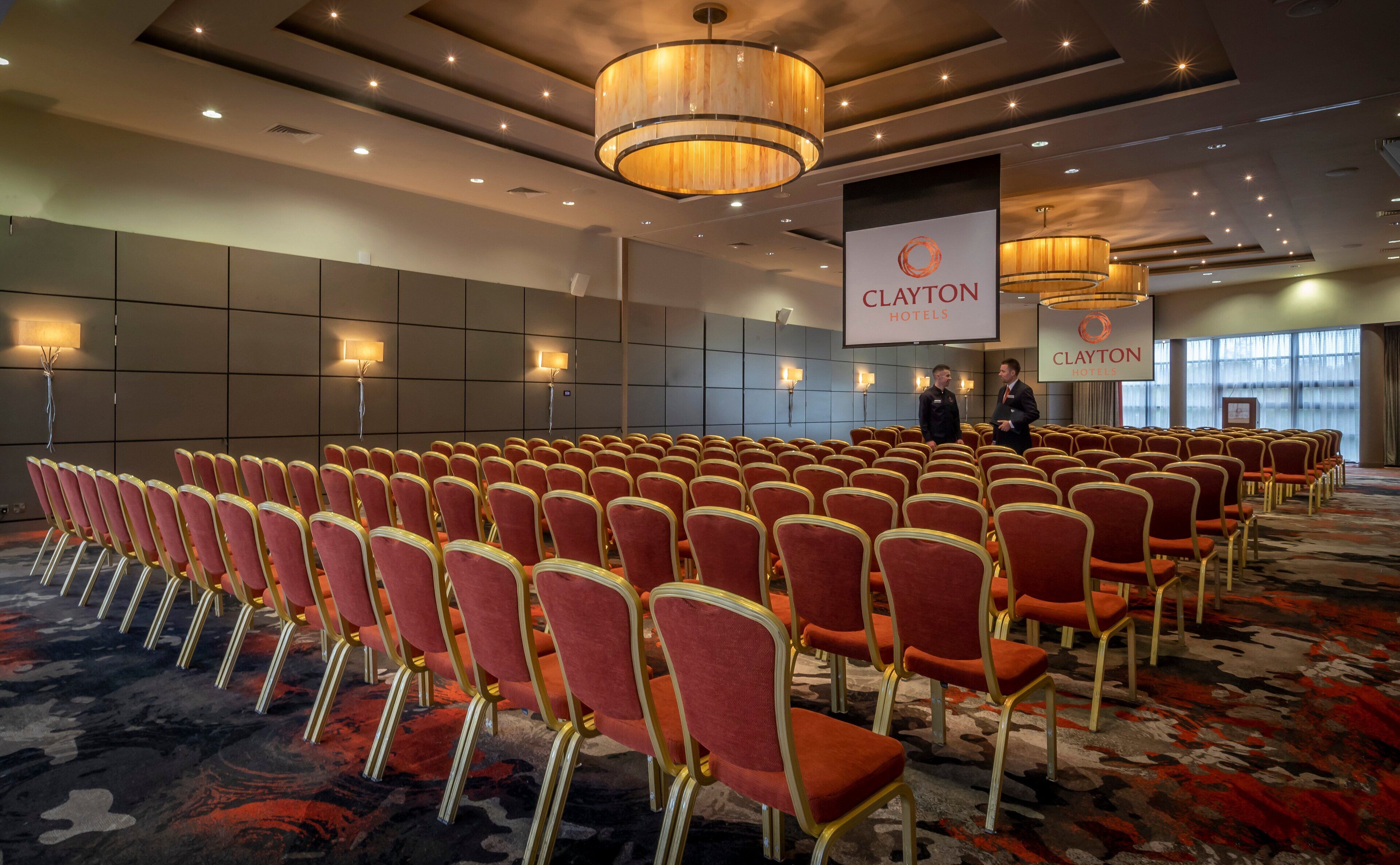 A conference room with rows of red chairs and a large screen displaying the Clayton Hotels logo.