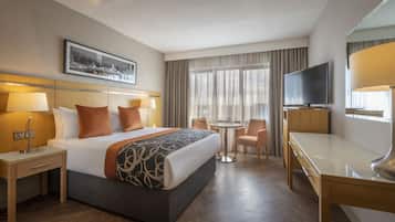 Une chambre d’hôtel comprenant un lit, des tables de chevet, un bureau, une chaise, un téléviseur et une fenêtre avec des rideaux.