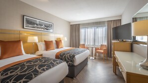 Habitación de hotel con dos camas, un escritorio, una silla, un televisor y una ventana con cortinas.