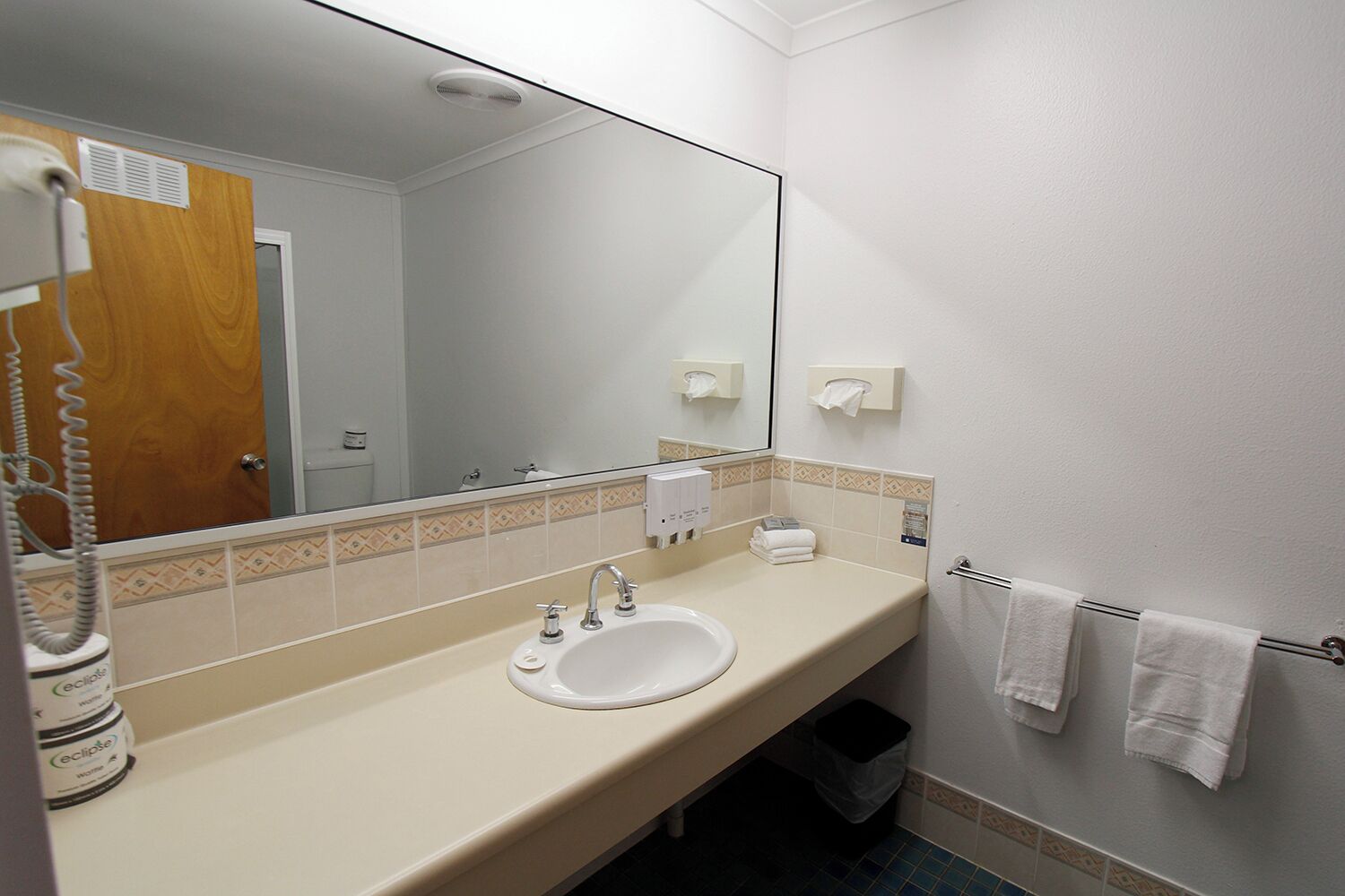 Une salle de bain équipée d’un lavabo, d’un miroir, d’un porte-serviettes et d’un sèche-mains.