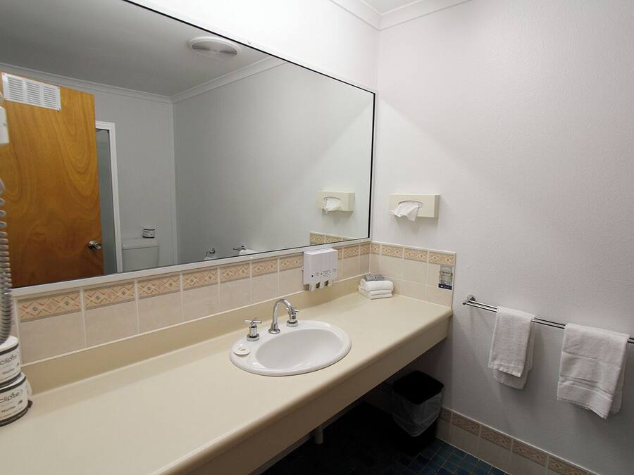 Une salle de bain équipée d’un lavabo, d’un miroir, d’un porte-serviettes et d’un sèche-mains.