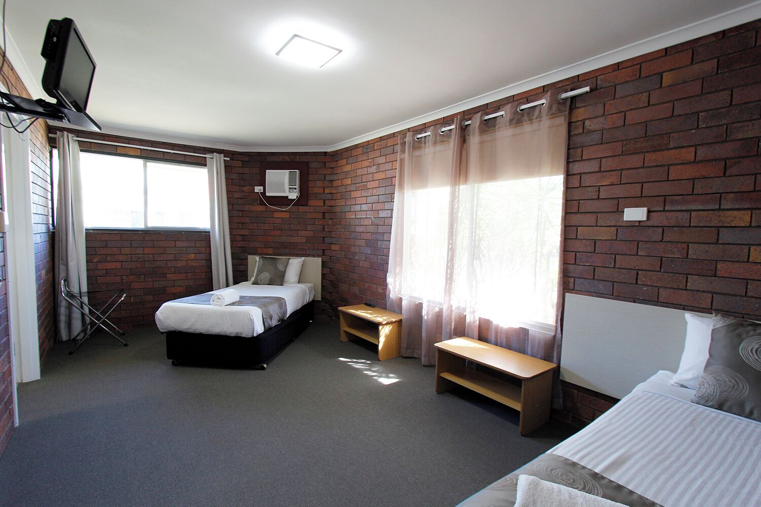 Un dormitorio con pared de ladrillo, una cama, un escritorio y un televisor sobre un soporte.