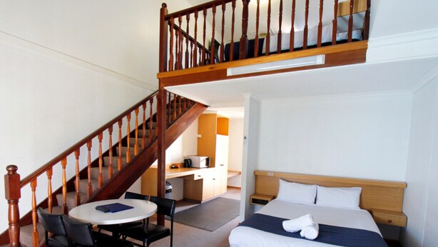 Une chambre à coucher avec un lit, un bureau, une chaise et un escalier.