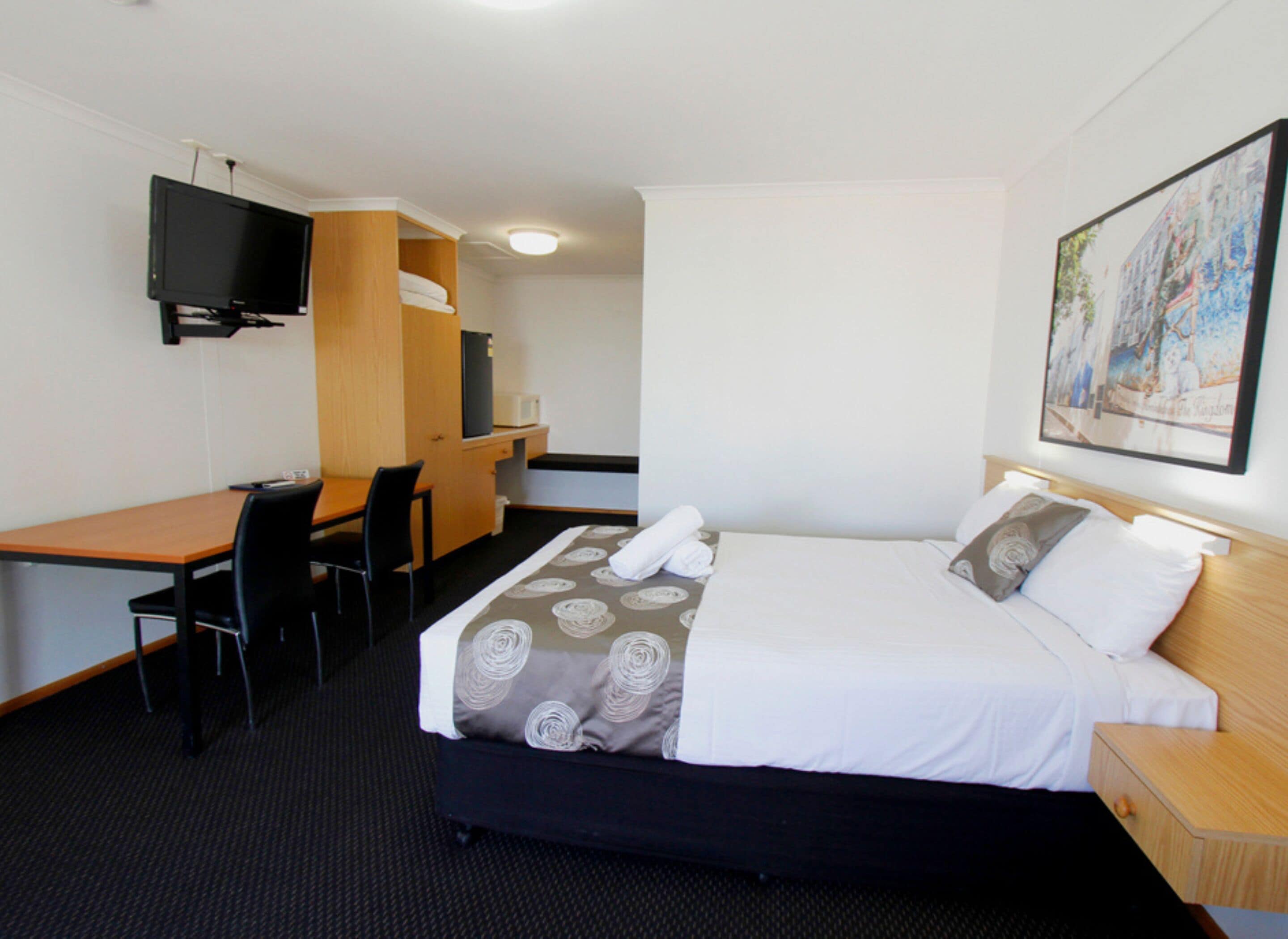 Una habitación de hotel con cama, escritorio, silla, televisor y un cuadro en la pared.