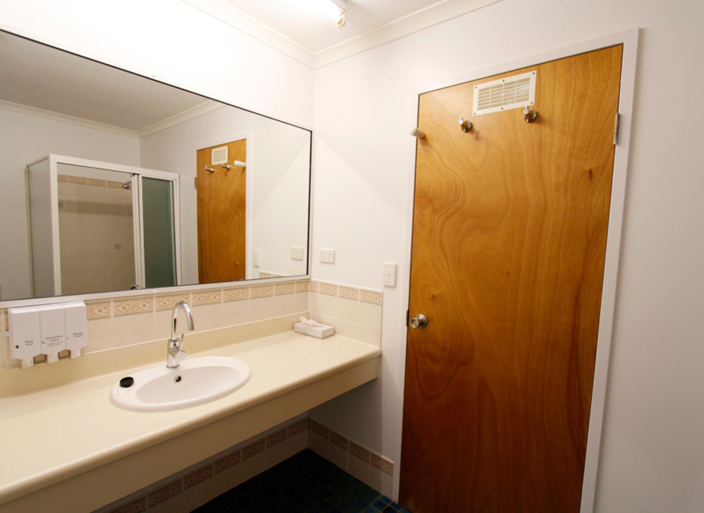 Un baño con lavamanos, espejo y puerta de madera.