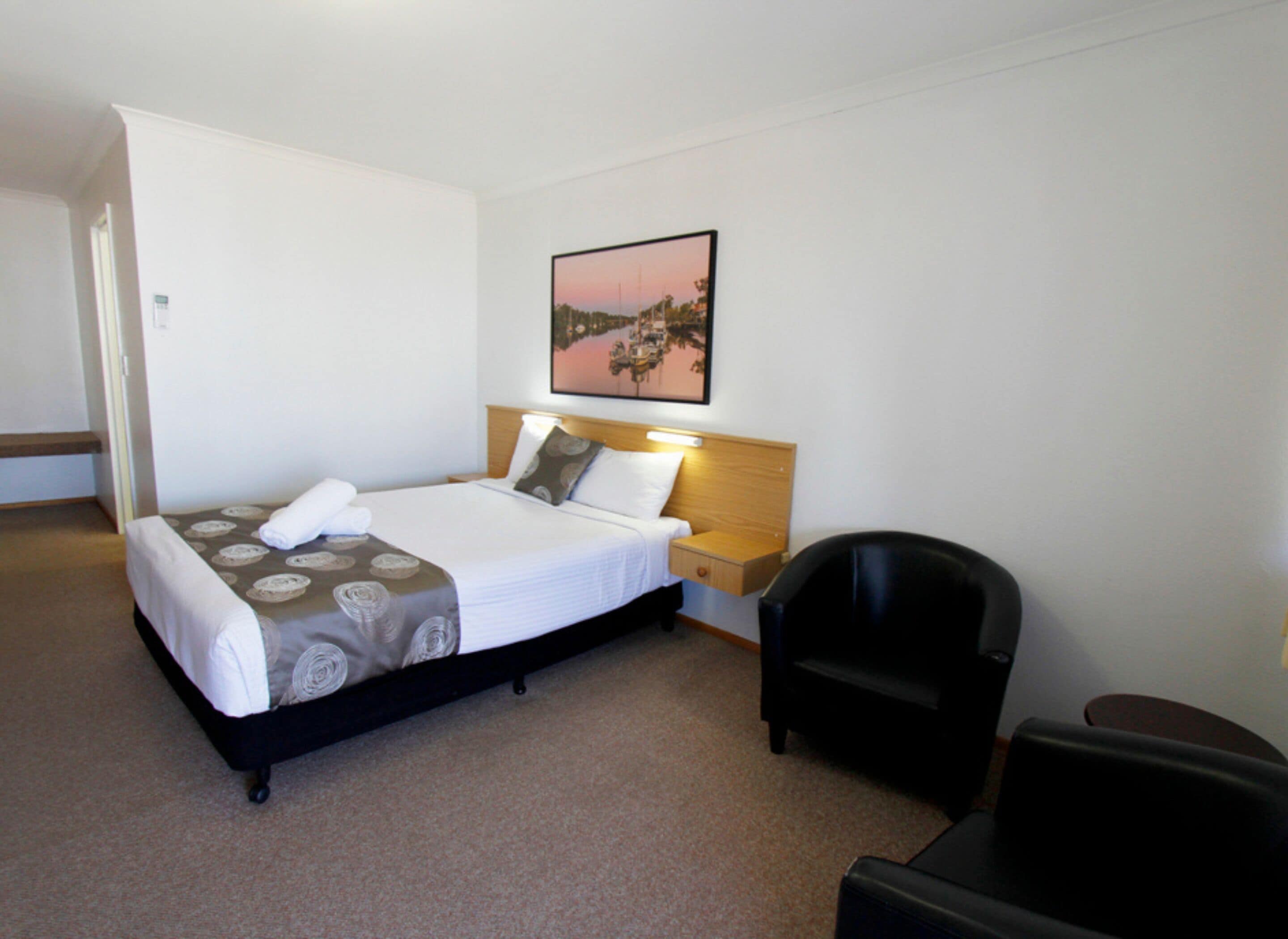 A hotel room with a bed, a nightstand, a chair, and a painting on the wall.