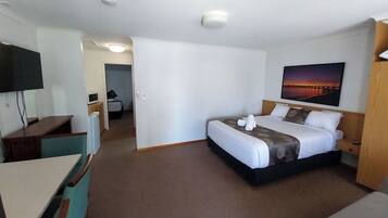 A hotel room with a bed, a desk, a TV, and a painting on the wall.