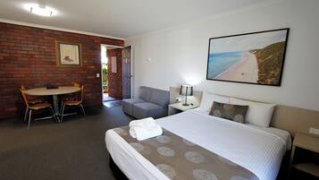 Ein Hotelzimmer mit Bett, Schreibtisch, Sessel, Sofa und einem Strandbild.